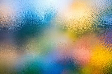 Colorful abstract blurry background with textured glass effect and vibrant hues of blue and yellow