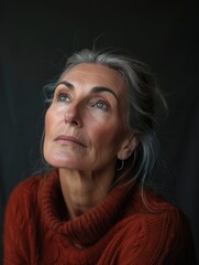 Fototapeta premium A woman with gray hair is wearing a red sweater and looking up. She has a serious expression on her face