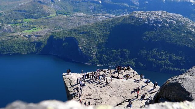 High angle view of people, hikers, tourists queueing for photos on corner spot on top of famous table like Pulpit Rock or Preikestolen in Norway on a beautiful sunny day.