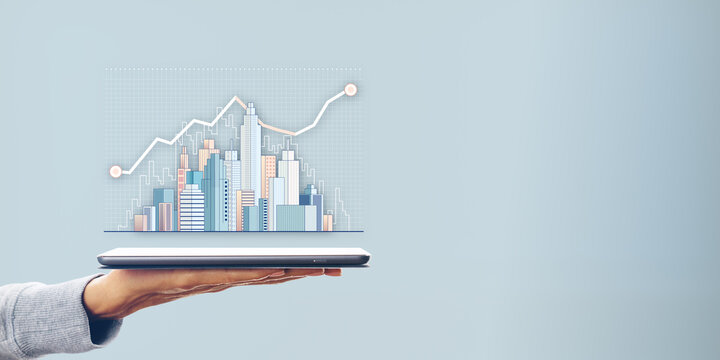 Hand holding a tablet displaying a city skyline with data charts on a plain blue background.