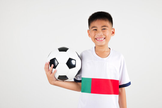A young boy is holding a soccer ball and smiling. The boy is wearing a white shirt with the number 7 on it
