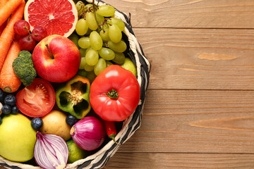 Wicker bowl with different fresh fruits and vegetables on wooden background, closeup