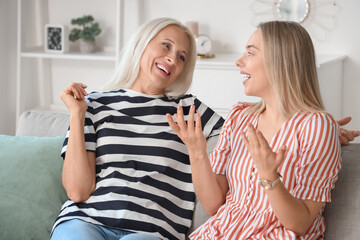 Happy young beautiful woman with her mother sitting on sofa in living room