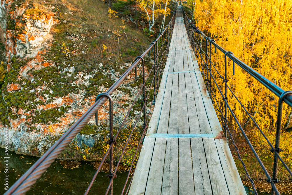 Wall mural a bridge over a river with a view of the trees and rocks below