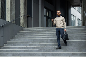Businessman confidently walking stairs holding smartphone, dressed in smart casual attire, in...