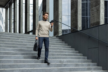 Business professional in modern outfit walking down city stairs using phone for important...