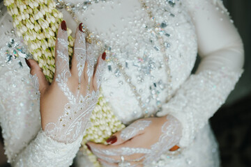 Bride Hands with white henna art tattoos holding bouquet flowers. Hands of bride girl with mehndi...