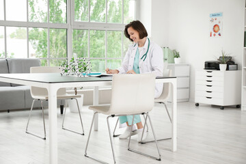 Female medical intern writing at table in clinic