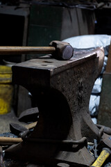 Close-up view of a vintage hammer resting on an anvil, set against a dimly lit workshop background, highlighting the textures and age of the metal tools.