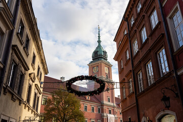 Historic clock tower and decorated Christmas wreath in Old Town Warsaw on a bright winter day. Concept of seasonal holiday atmosphere, cityscape, and Polish architecture. High quality photo