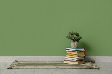 Stack of books and bonsai tree on floor near green wall
