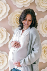 Portrait of a happy pregnant girl with a radiant smile, gently holding her belly. Ideal for showcasing the beauty of motherhood, pregnancy journeys, and family-related themes.