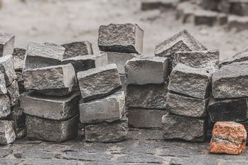 A stack of cobblestones for a sidewalk. Removed paving stones. Time to scatter and collect stones. Stone road. Repair works. Paving stones in a pile. Bricks under construction.