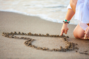 woman drawing a heart on the sand at sunset in a summer love concept