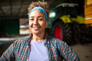 Portrait of a female farmer standing confidently in front of tractor in barn