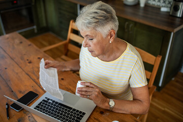 Elderly woman reading medication instructions while using laptop
