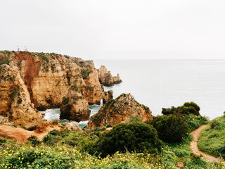 Scenic coastal cliffs covered in greenery, with dramatic rock formations jutting into the calm ocean