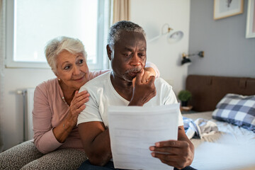 Obraz premium Senior couple reviewing bills with concerned expressions in bedroom