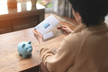 A Woman Reviews Paperwork by a Piggy Bank in a Cozy Living Room Filled With Natural Light
