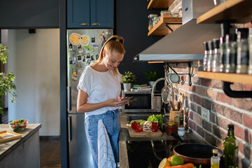 Smiling young woman using smartphone in modern kitchen