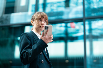 Fototapeta premium Young Professional Woman Using Her Smartphone Outside a Modern Office Building in the City at Midday