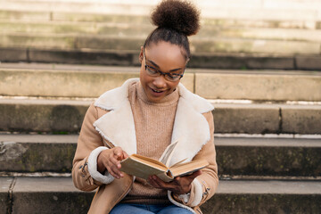 Obraz premium A Young Woman Enjoys Reading a Book While Seated on Stone Steps in a Cozy Autumn Afternoon