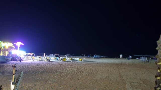 Night timelapse shot of calangute beach goa with people rushing about, relaxing on the beach on recliners and enjoying the music from the brightly lit shacks