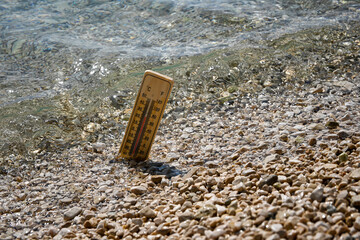 Wooden thermometer measuring increasing temperature of sea water during heat wave