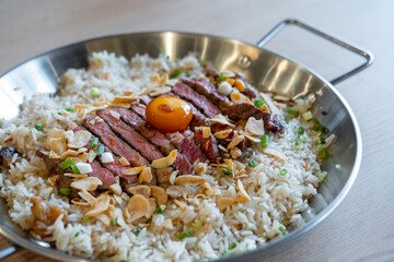 Beef with garlic fried rice, a dish of rice topped with rare beef served with pickled egg yolk with fish sauce on a pan