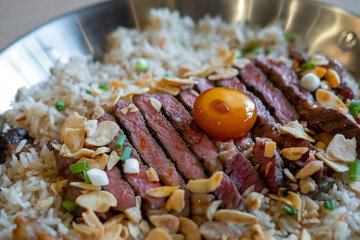 Beef with garlic fried rice, a dish of rice topped with rare beef served with pickled egg yolk with fish sauce on a pan