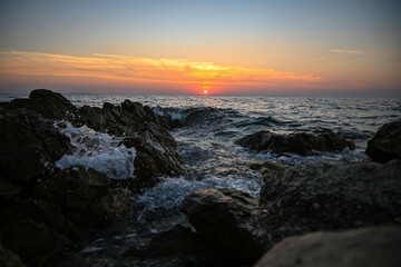 Obraz premium Ocean waves crashing on rocks with a beautiful sunset in the background
