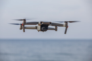 a gray drone flies in the sky over the sea