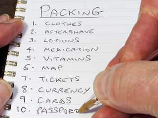 Closeup of a hand using a pen to write in a notebook a numbered packing list of items for business or leisure travel.