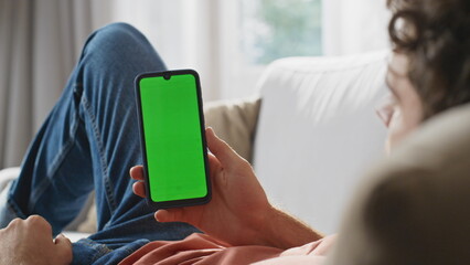 Man hands watching greenscreen cellphone at sofa closeup. Guy holding smartphone