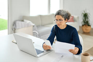 Mature lady paying bills online checking medical invoices receipts bills making baking payments or...