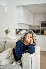 Happy relaxed 50 years old woman laying on sofa at home. Smiling mid aged lady relaxing in living...