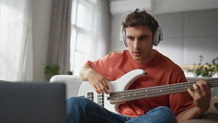 Guitar teacher recording tutorial at cozy sofa closeup. Happy guy looking laptop