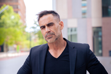Obraz premium Close-up of a caucasian businessman looking angry at the camera in a suit standing in outdoor workspace. Front view of a young lawyer with thoughtful expression staring
