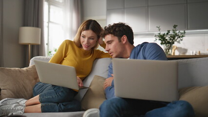 Young couple cooperating computers at living room closeup. Colleagues working