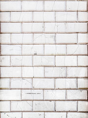 Close-up of a weathered white subway tile wall background, showing cracks, stains, and imperfections. The vintage texture reveals signs of age and wear in an urban setting.