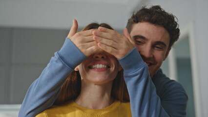 Smiling husband closing eyes of woman at home closeup. Happy man making surprise