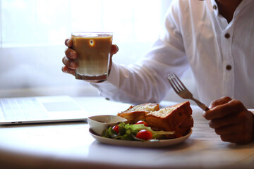 Breakfast is arranged on the desk of a man who is sitting and working and eating breakfast, with a...