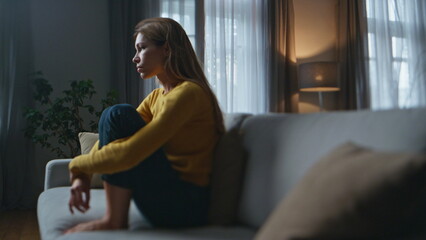 Depressed woman thinking problems at evening home. Frustrated girl sitting sofa