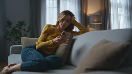 Heartbroken girl messaging smartphone dark house. Depressed lady sitting couch