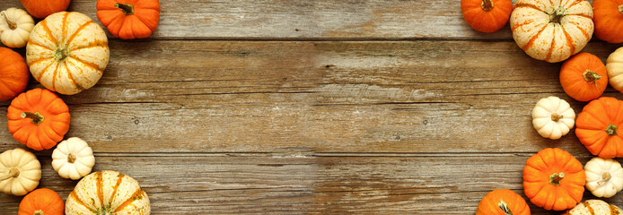 Fall double border of orange and white pumpkins over a rustic wood banner background. Top view with copy space.