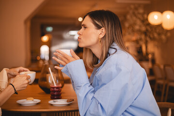 Communication and friendship concept - smiling young women sisters friends with coffee cups at cafe laughing and talking, they have good time together. Happy smiling girls gossiping.