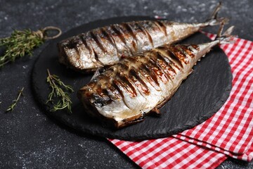 Delicious grilled mackerel, thyme and napkin on dark textured table, closeup