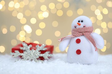 Funny snowman figure and decorative snowflake on artificial snow against blurred lights