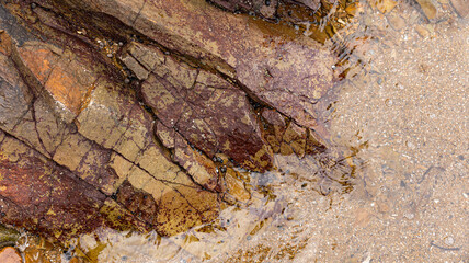 A Beautifully Textured Rock Formation by the Shoreline with Soft Sand and Glimmering Water