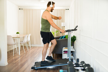 Fototapeta premium Happy man staying active, enjoying music and monitoring his progress while exercising on a home treadmill
